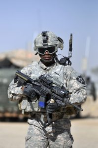 A U.S. Soldier conducts a walk-and-talk through a market in Nassir Wa Salaam, Iraq. He is carrying an M4 Carbine. Image courtesy of DoD.