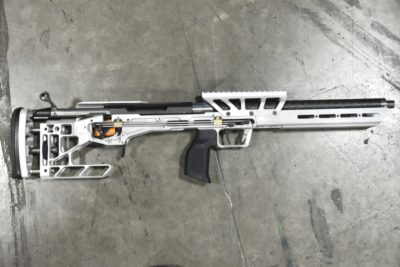 An aluminum, bullpup rifle rests on a concrete background.