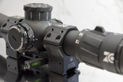 A black rifle scope on a white marble background.