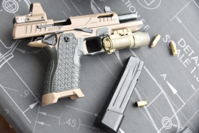 A tan pistol sitting on a black desk. Bullets lay on the table around it.