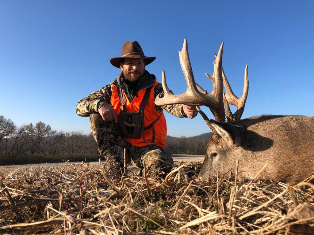 Hunter in camo and orange posed next to beautiful buck