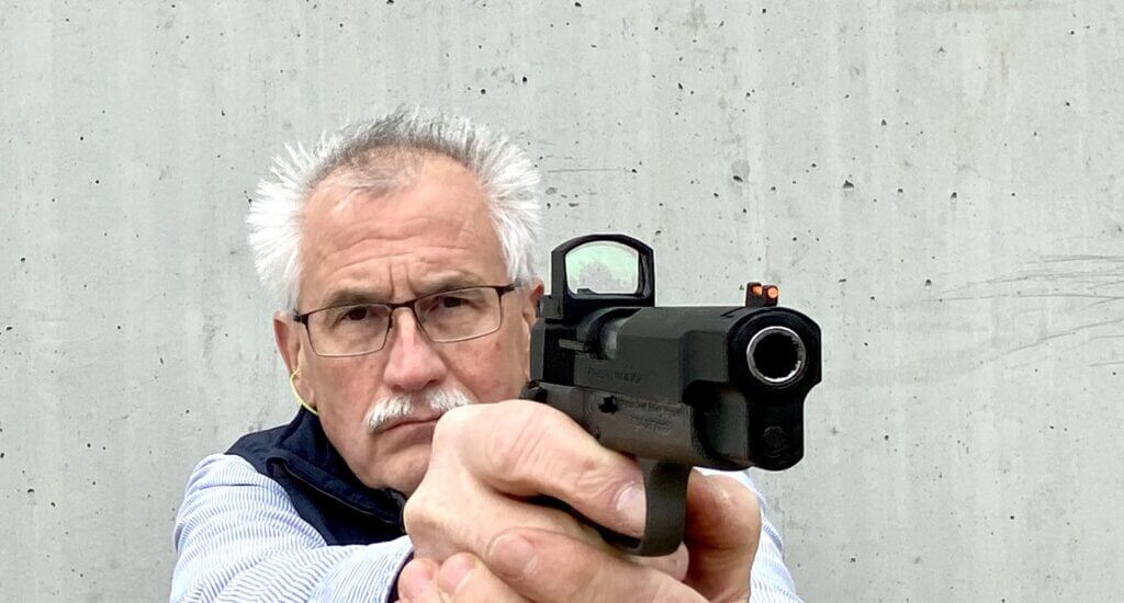 Shooter aiming down the barrel of a pistol with the Samaritan red dot attached