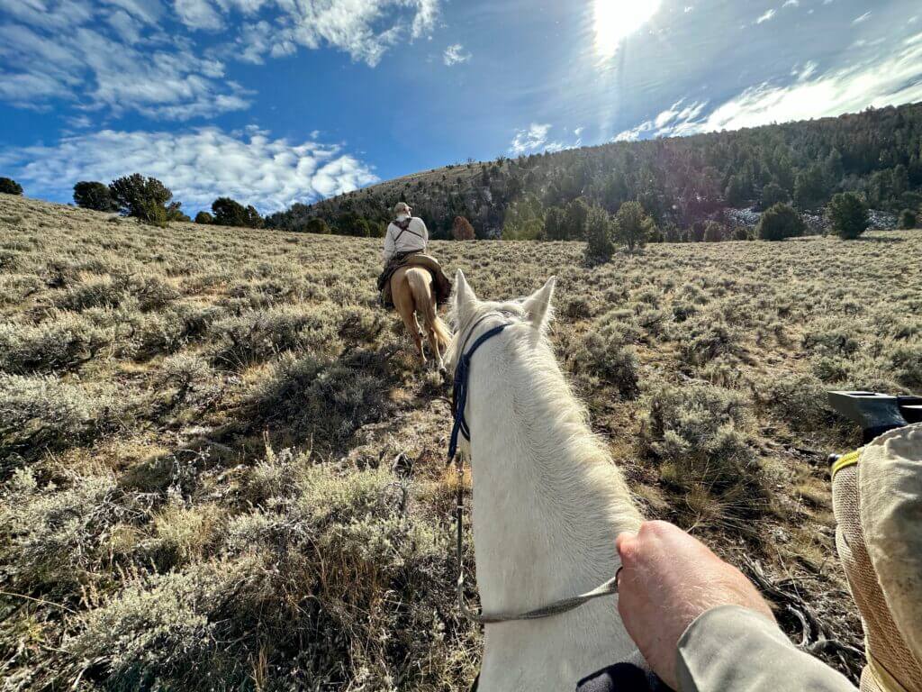 Hunters ride on horses toward the mountain top.