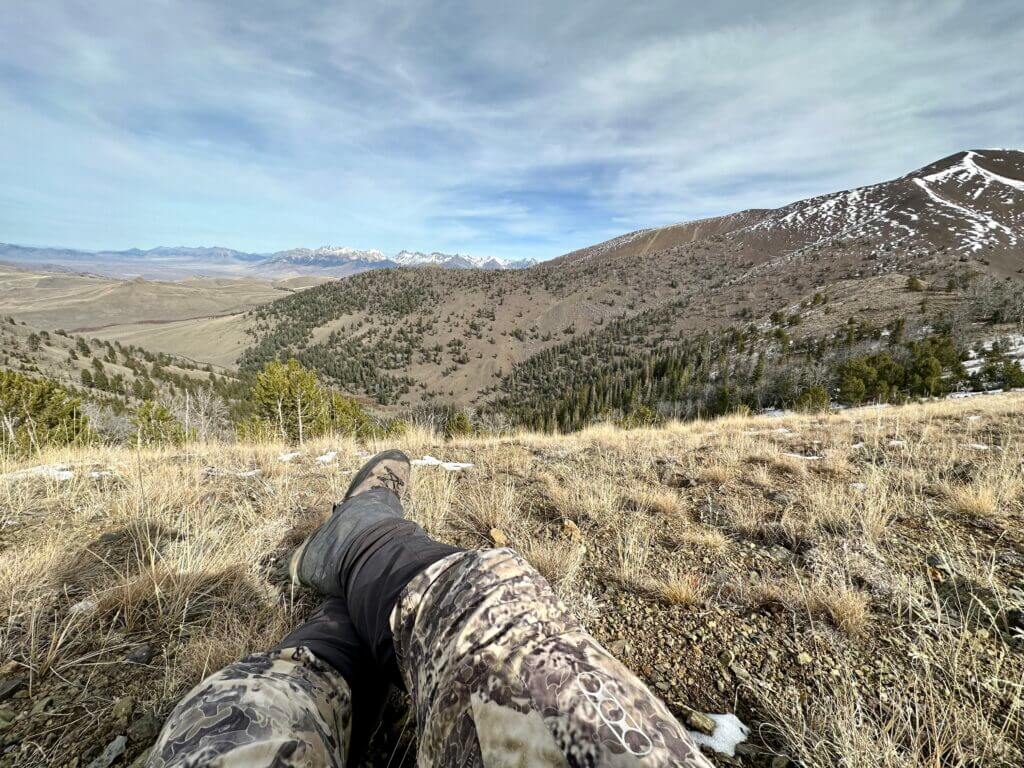 Relaxing on a hill, a hunter lays with his legs crossed while the sun is high in the sky.