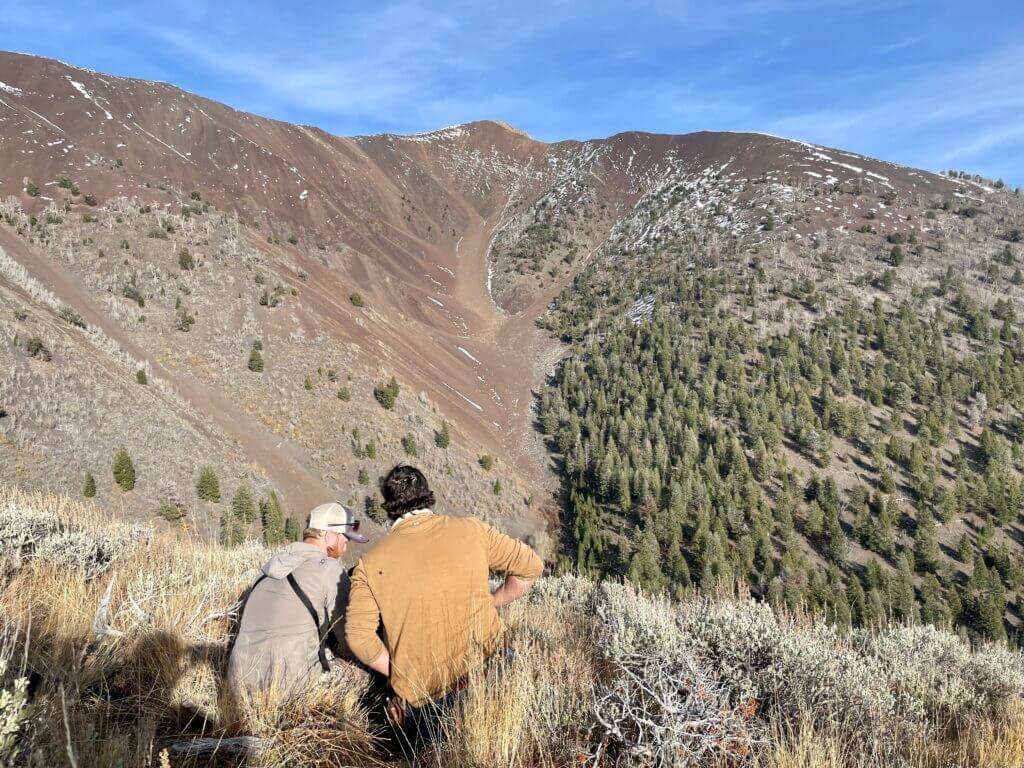 Two hunters fuss with equipment while they prepare to take a shot across a large canyon.