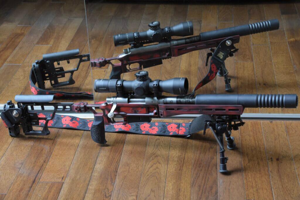 A red rifle with suppressor sits in front of a mirror.