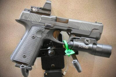 A handgun with red dot and flashlight is posed against a brown background.