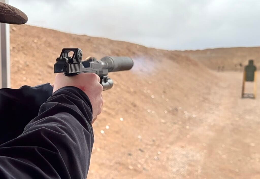 A man shoots a suppressed handgun at the gun range.