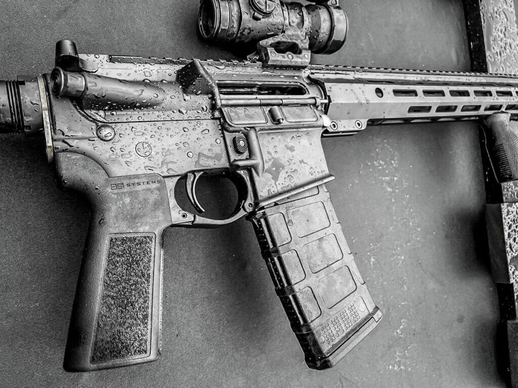 This is a closeup of a rain covered AR-style rifle on a black table.