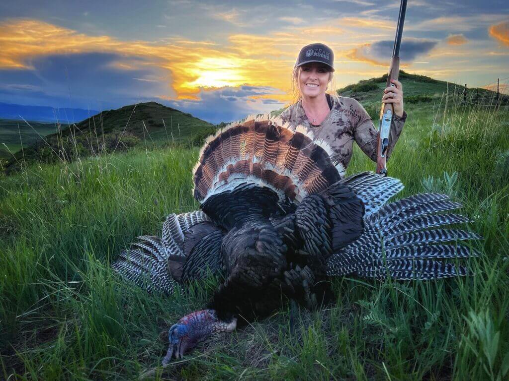 Woman with turkey and shotgun out in the mountains with sunrise