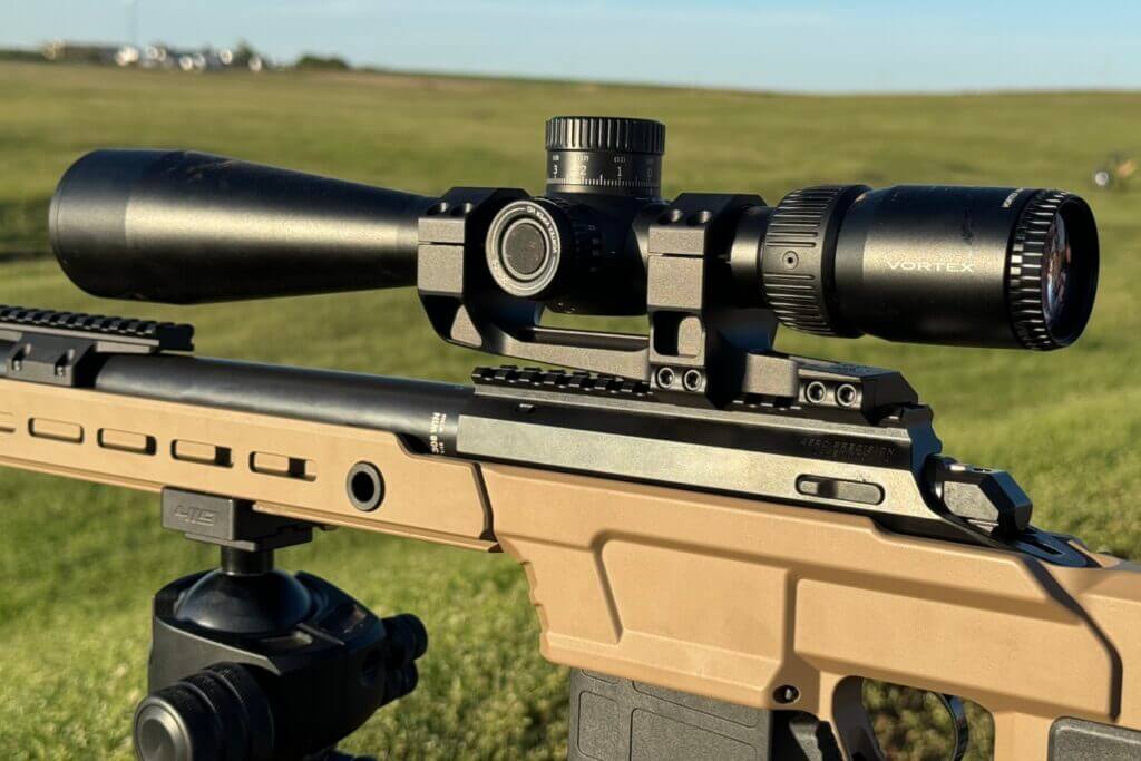 A scope mounted to a rifle in front of a vibrant green field