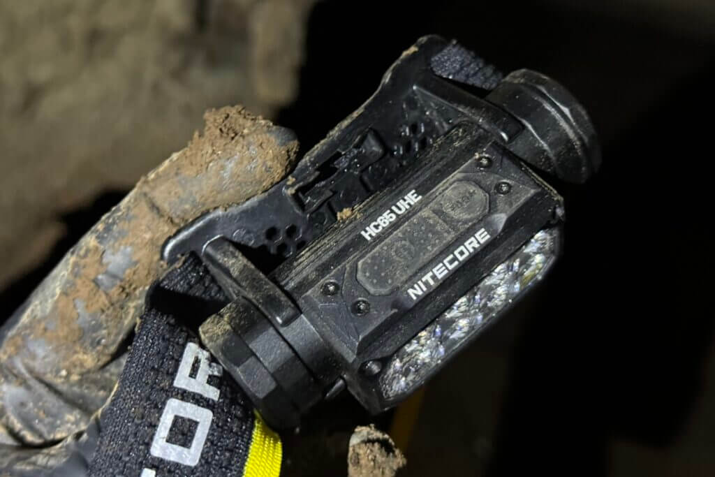 A dirty glove holding the Nitecore HC65 UHE headlamp in a dark cave