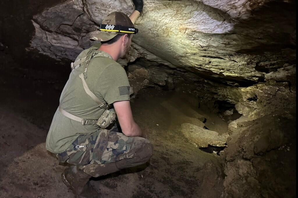 Man in camo looking into a dark cave with the Nitecore HC65 UHE headlamp