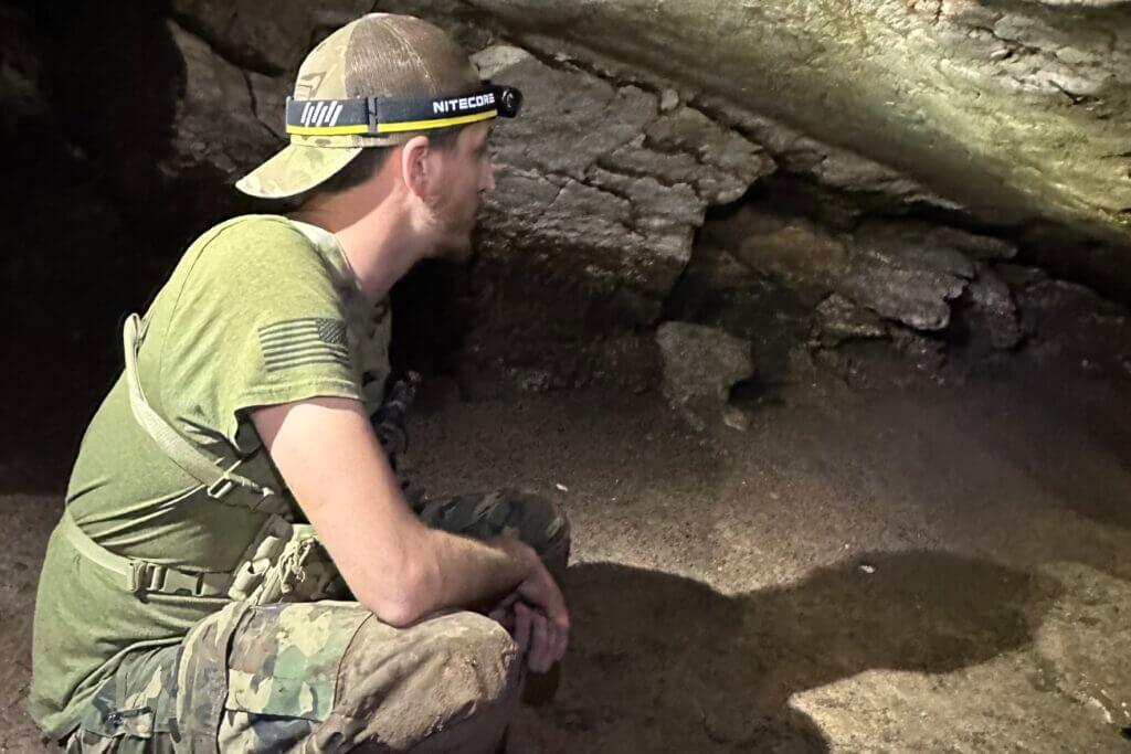 Man in camo using Nitecore HC65 UHE headlamp in a dark cave