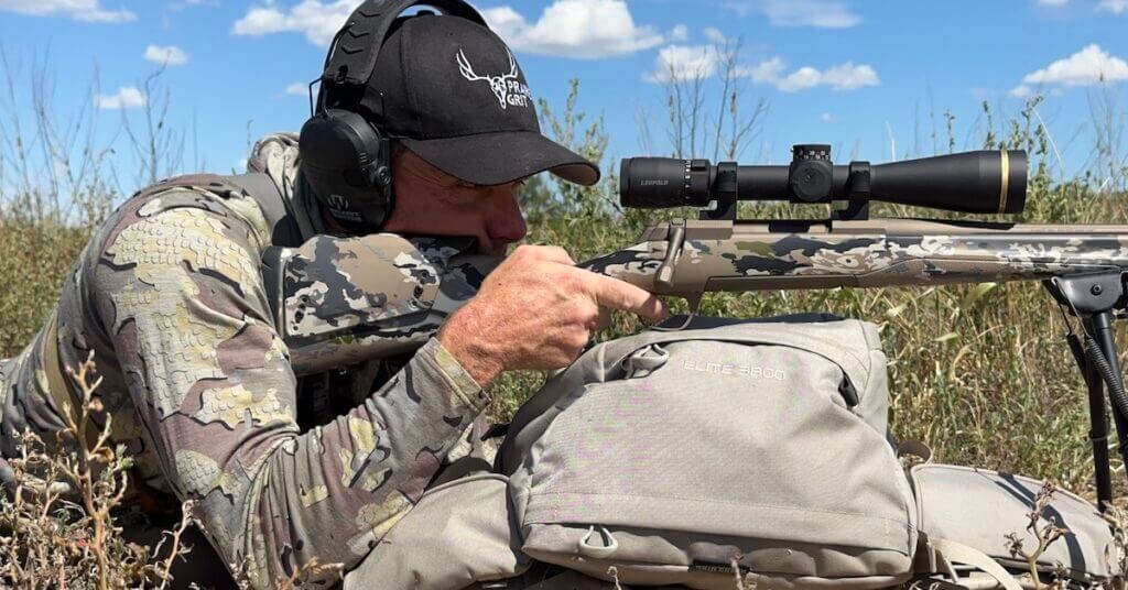 Man in camo shooting camo rifle with range bags and black scope