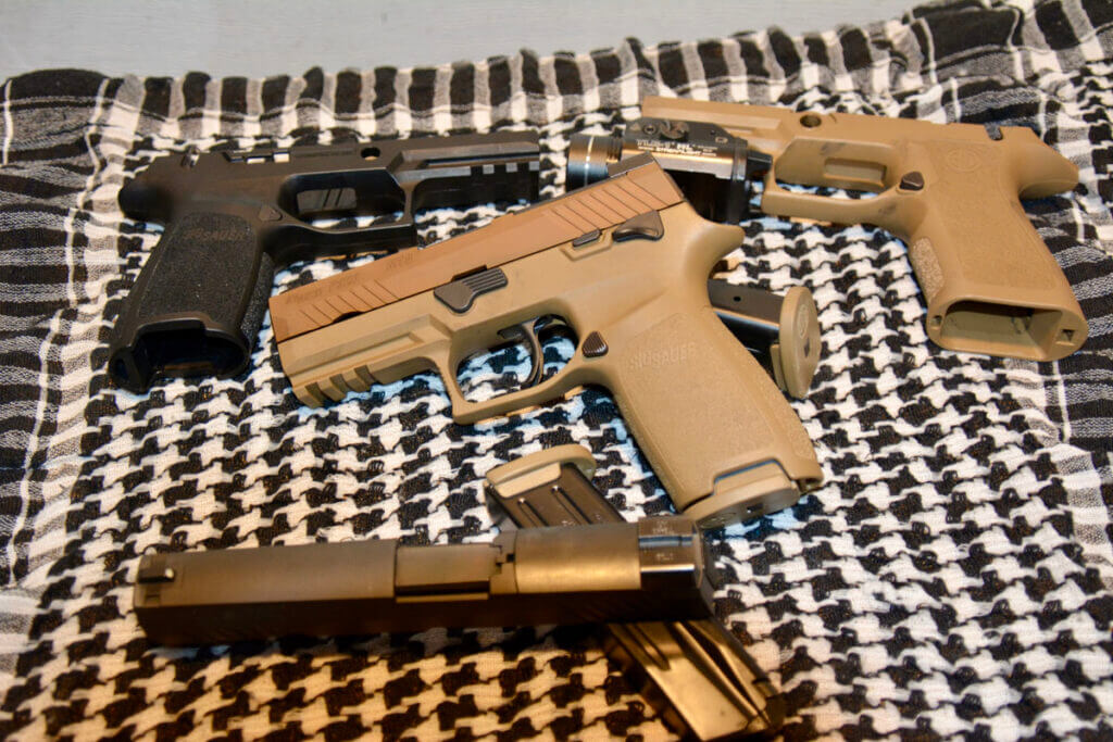 Pile of Sig Sauer handguns resting on checkered blanket with magazines and accessories