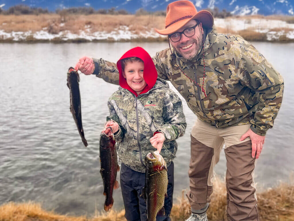 Man and boy holding three large trout by the mouths.