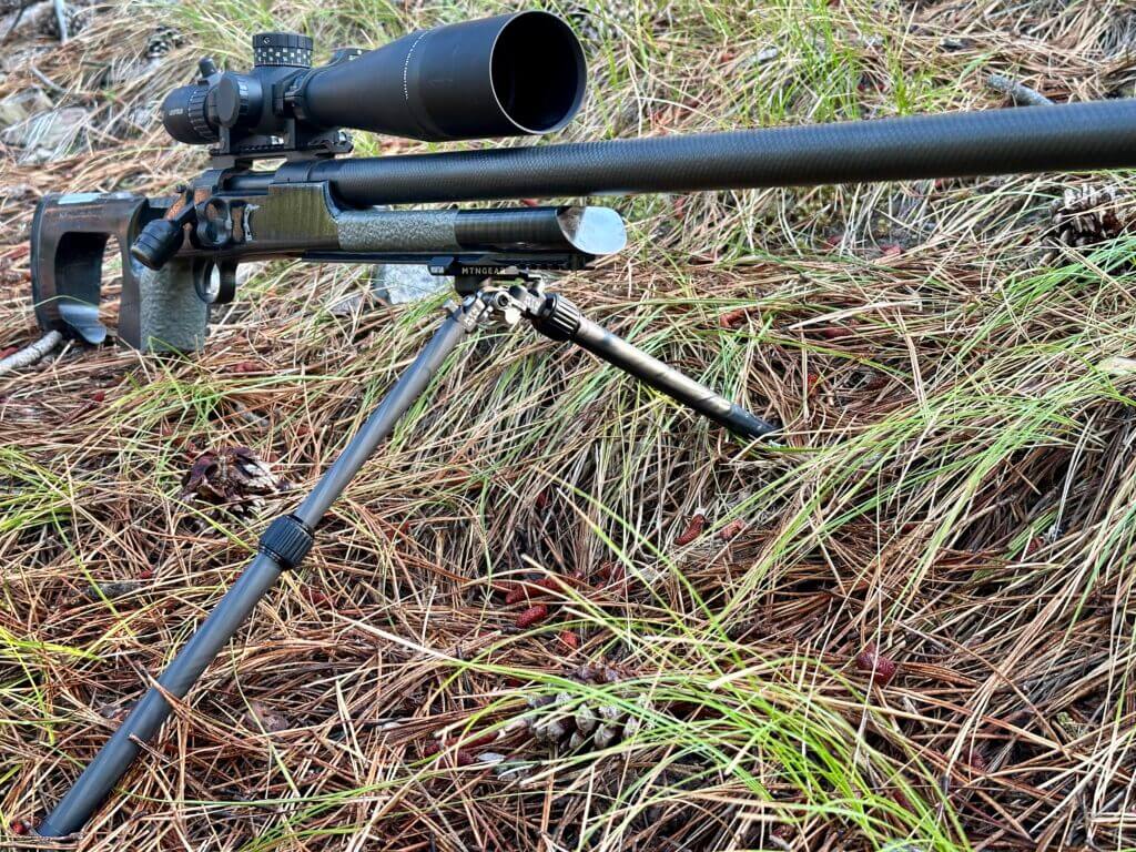 A black rifle with the Mountain Bipod sits on a grassy hill.