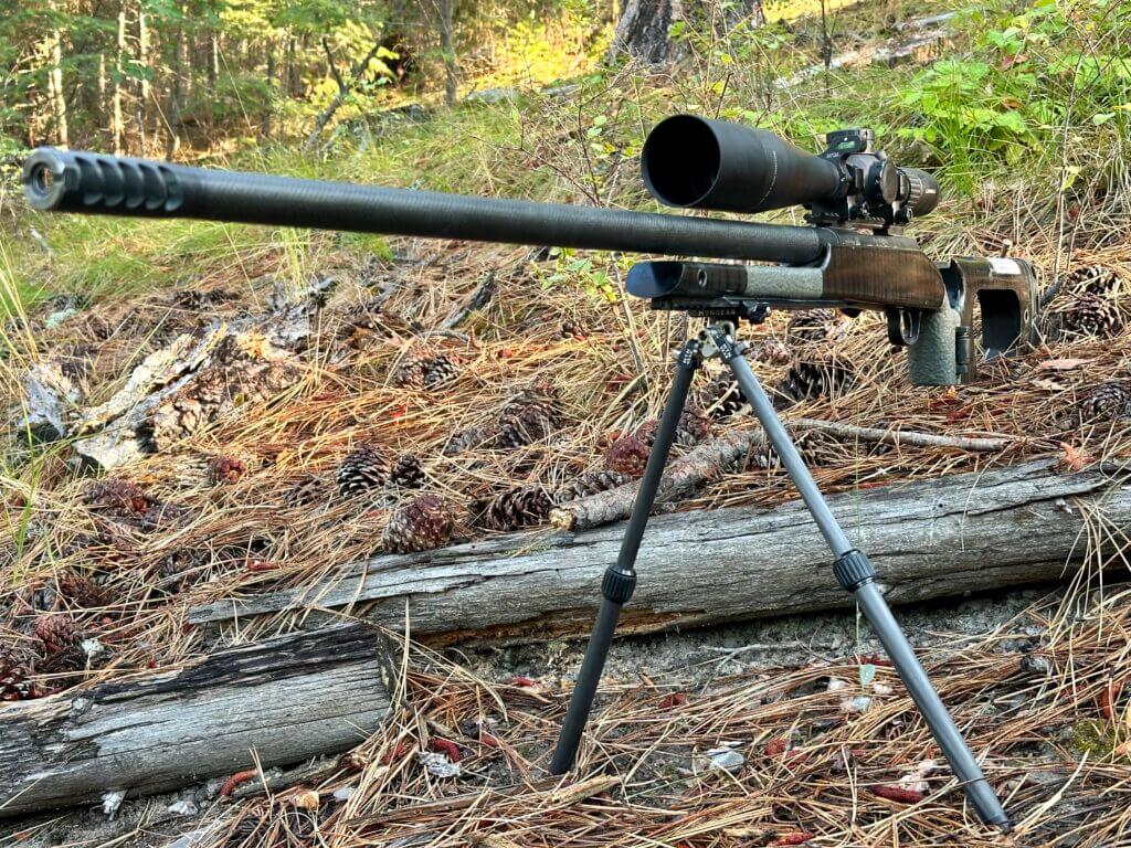 A rifle sits on a bipod in the grass-covered mountains.