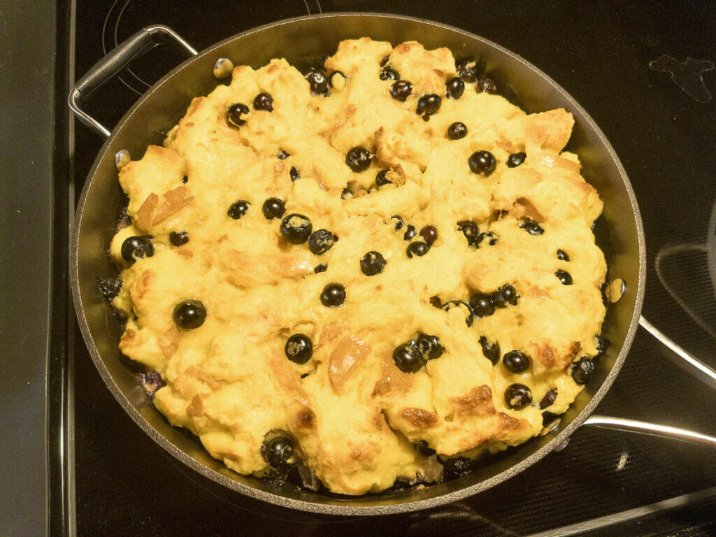 A cast iron skillet filled with egg and bread french toast bake with blueberries.