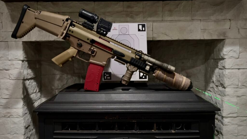 A rifle with laser training device sits on a stove in front of a target.