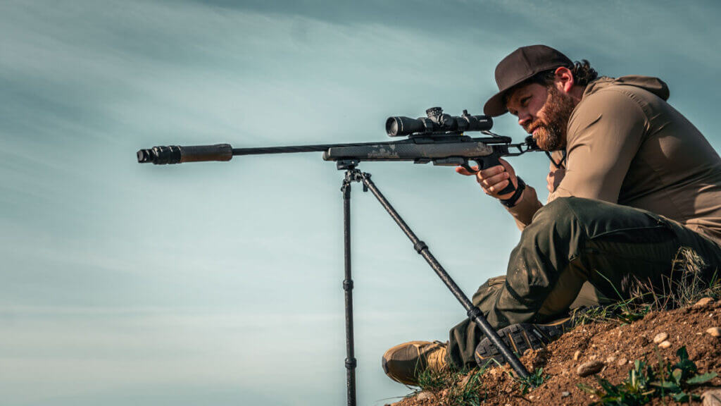 man with a rifle and a bipod sitting on a hill