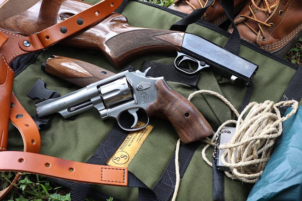 smith & wesson 617 mountain gun with a browning sa-22, rope, flint striker, holster, and poncho