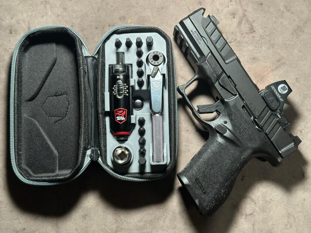 A handgun with an optic is next to a tool kit.
