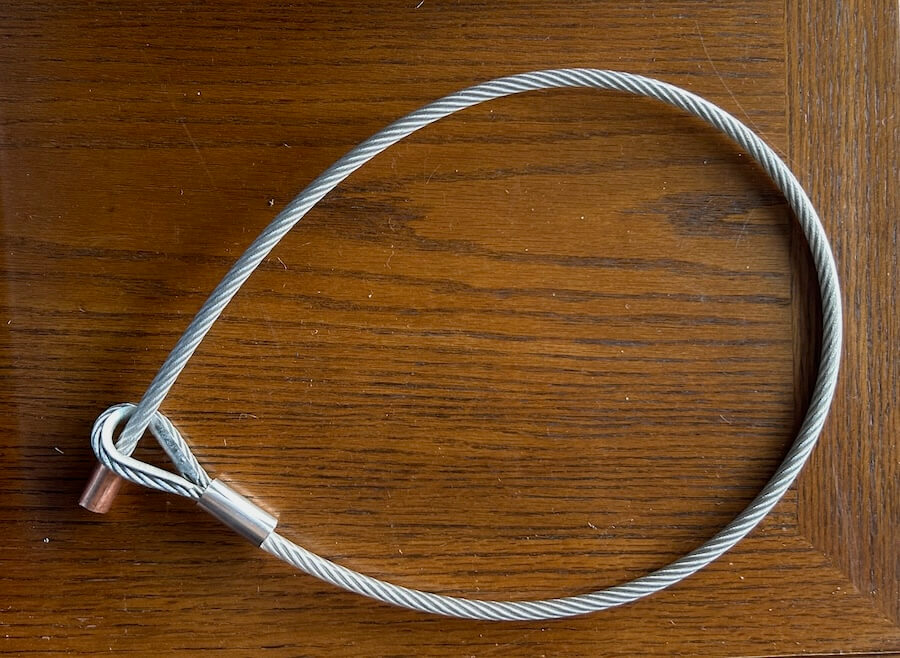 Steelhead Outdoors security cable looped and coiled on a wooden surface.