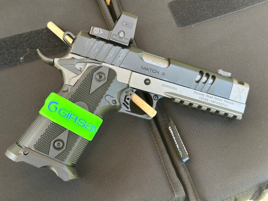 A black and silver handgun with an optic is posed against a black background.