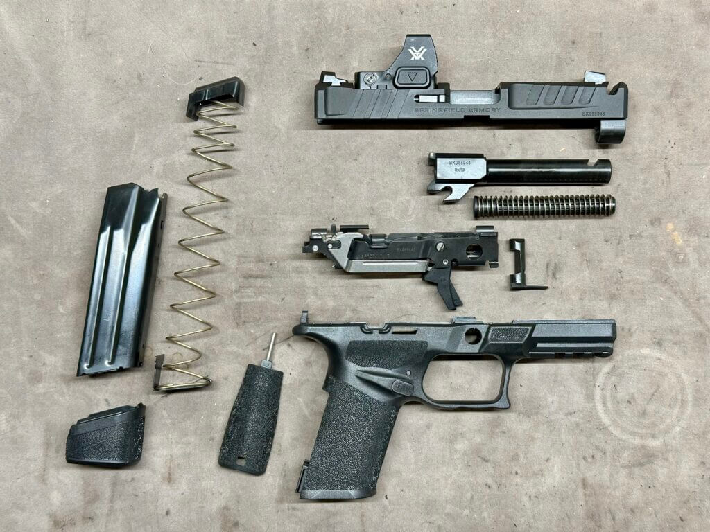 Disassembled completely, a handgun is laid out on a tan tabletop.  Echelon 4.0C Comp
