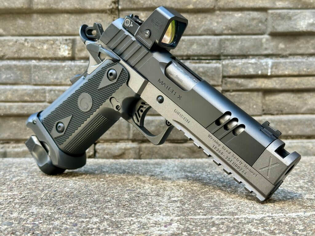 A handgun with an optic on it is posed in front of a stone wall.