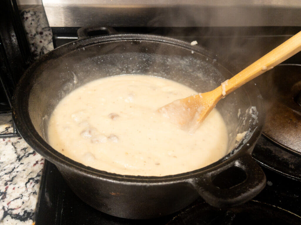 Cast iron pot of elk heart mashed potato soup on the stove with wooden spoon.
