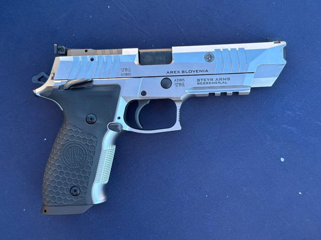 A silver gun sits on top of a blue table. It has black accents.