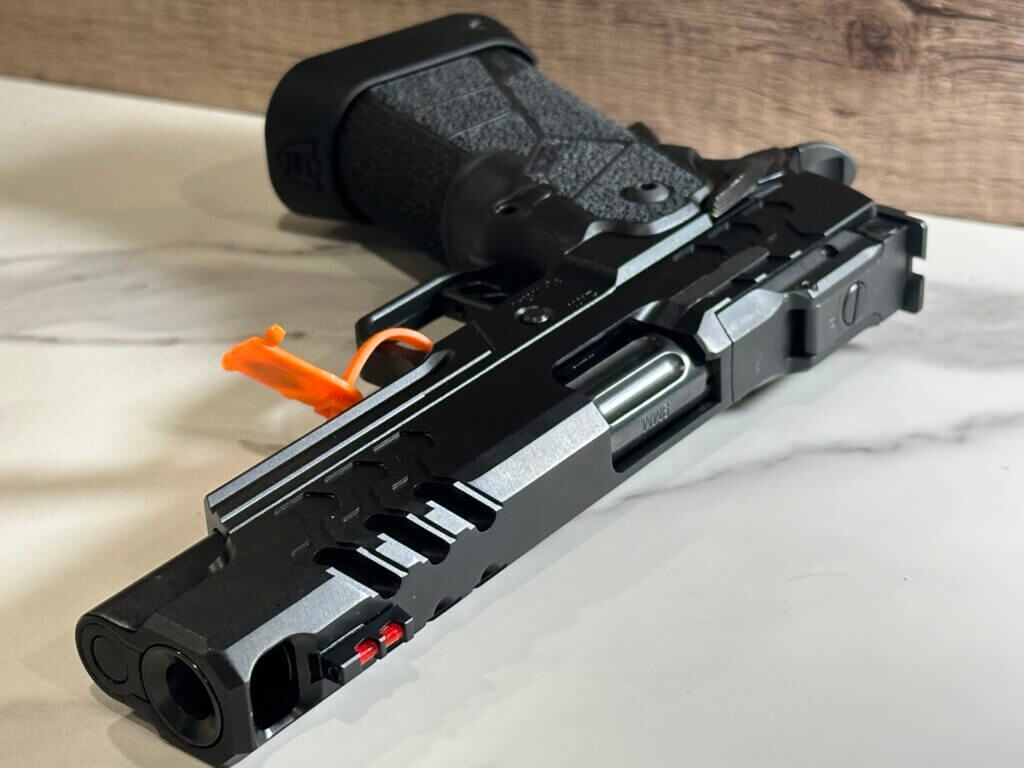 There is a black handgun with the muzzle facing toward us laying on a white granite countertop. This handgun has a big port in the slide and barrel right behind the muzzle.