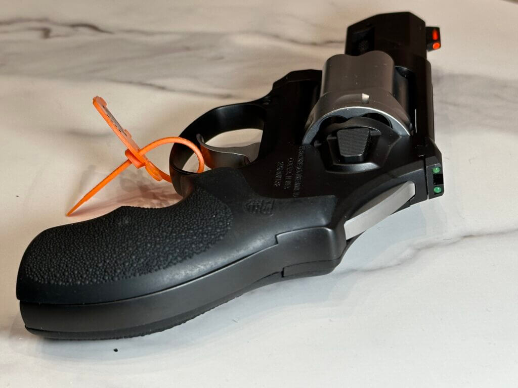 A black revolver lays on a white marble table, facing away from us.