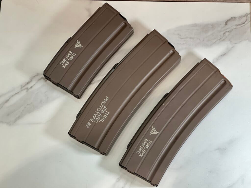 There are three tan rifle magazines laying on a white marble table.