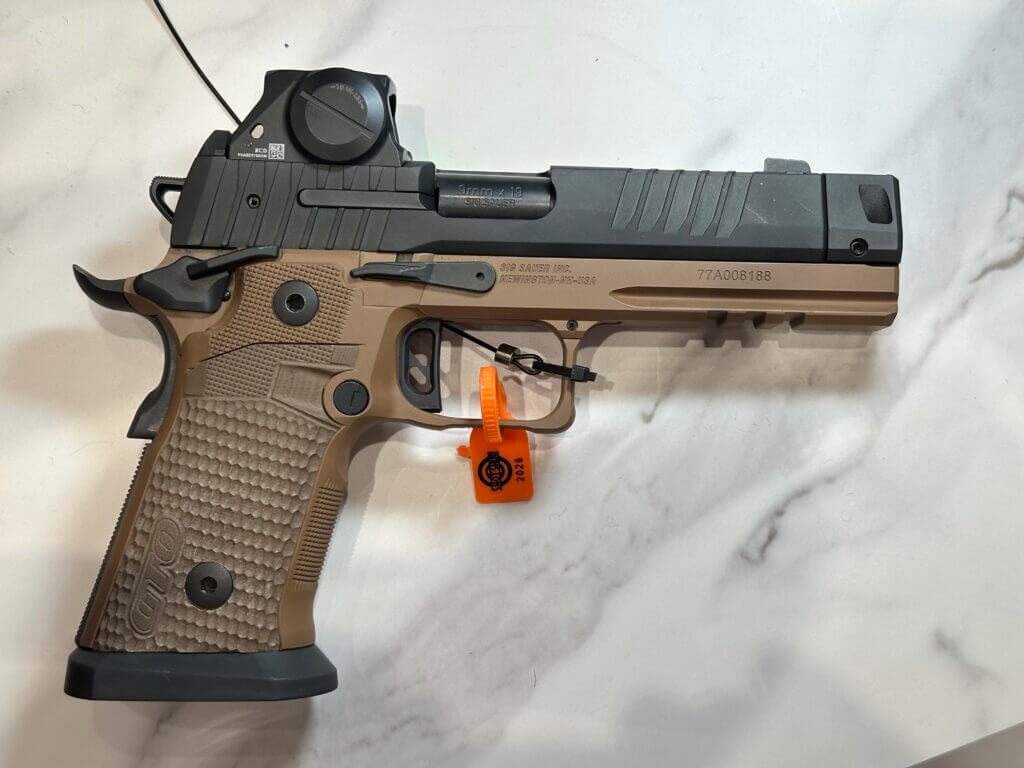 A tan and black handgun rests on a white marble countertop.