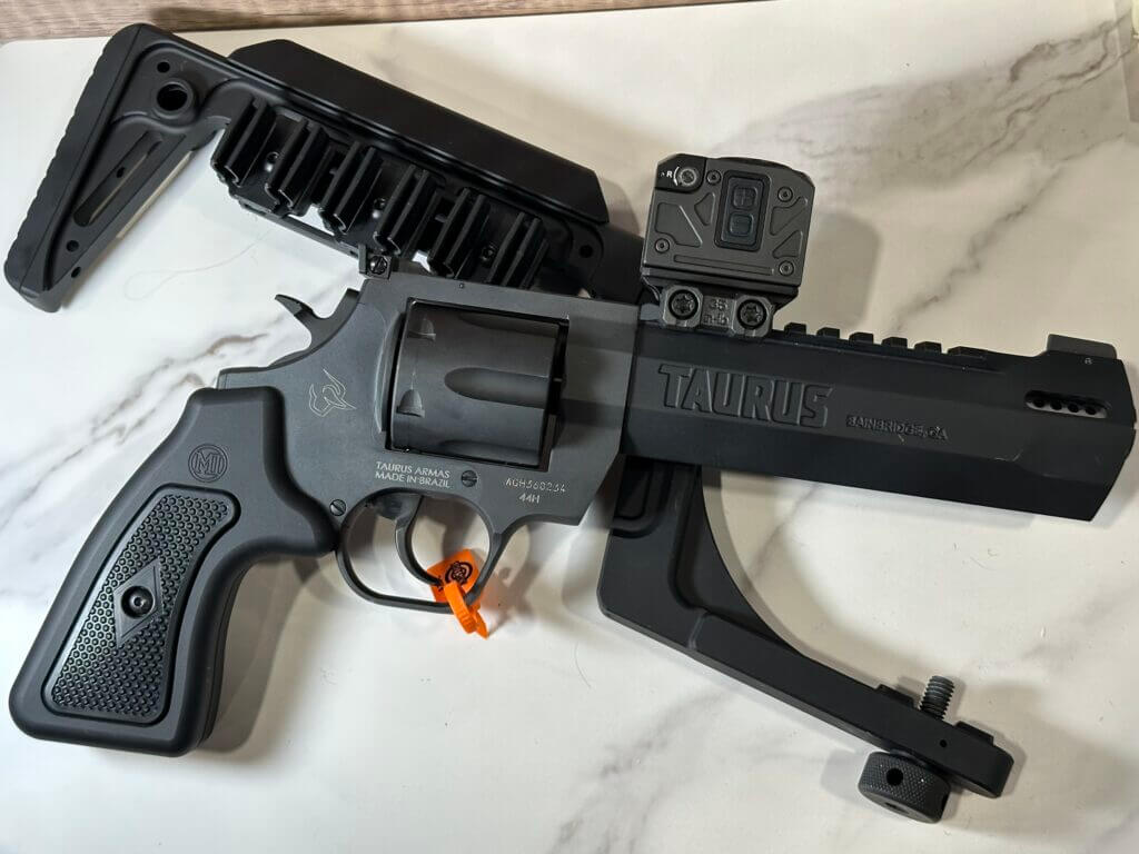 A revolver is laying on top of a removable buttstock. both lay on a white granite background.