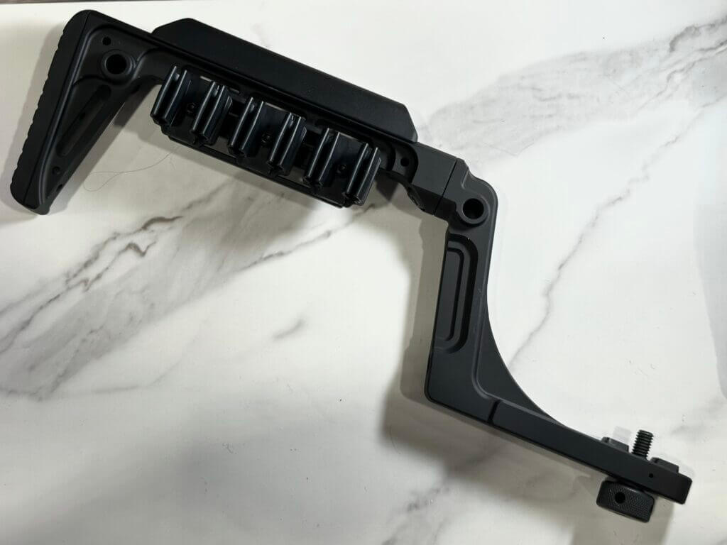 A black buttstock with a shell quiver on it lays on a white granite background.