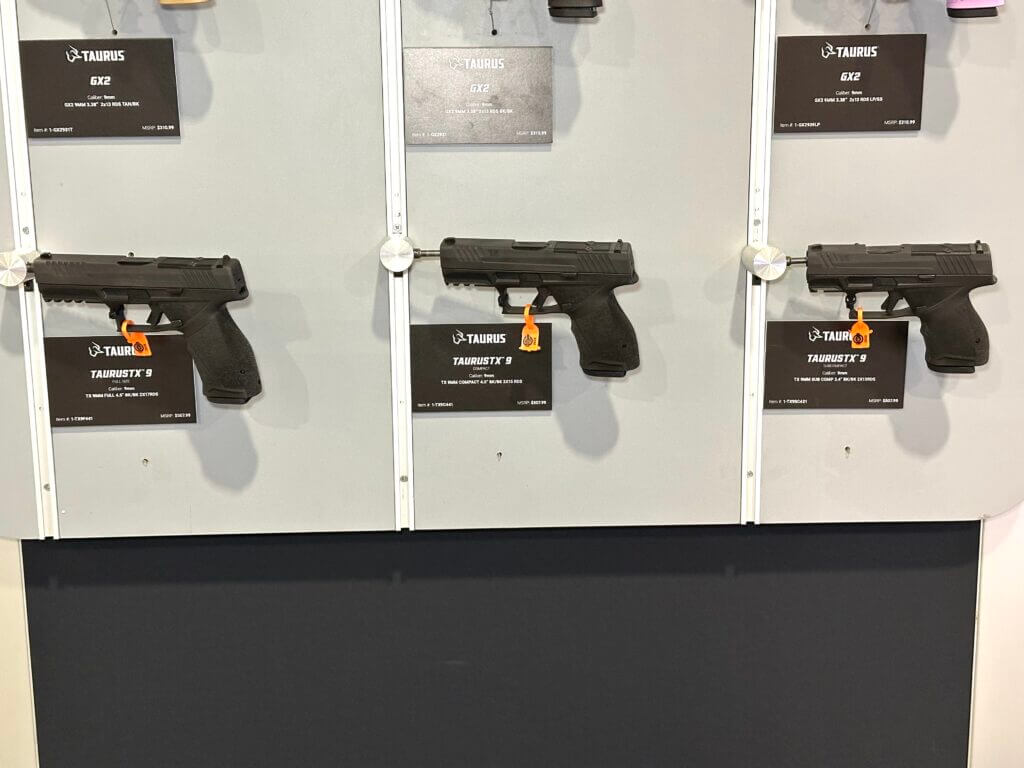Three different pistols are hanging off of a wall display. They are arranged in order of biggest to smallest.