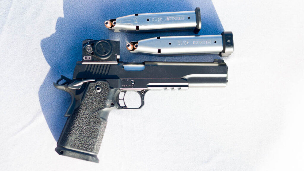 The gun laying on a table facing right with the right side up with two magazines arranged above in on the table.