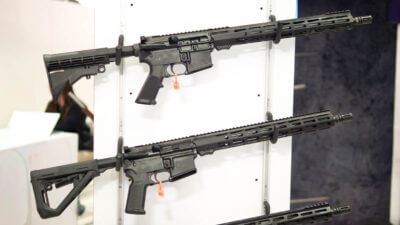 two AR-15s hanging on a white wall rack pointing right.