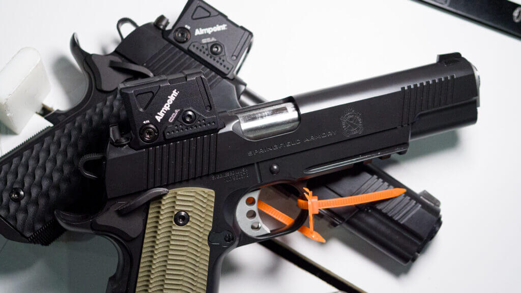 two 1911s laying on top of each other on a white table facing right with COA sights.