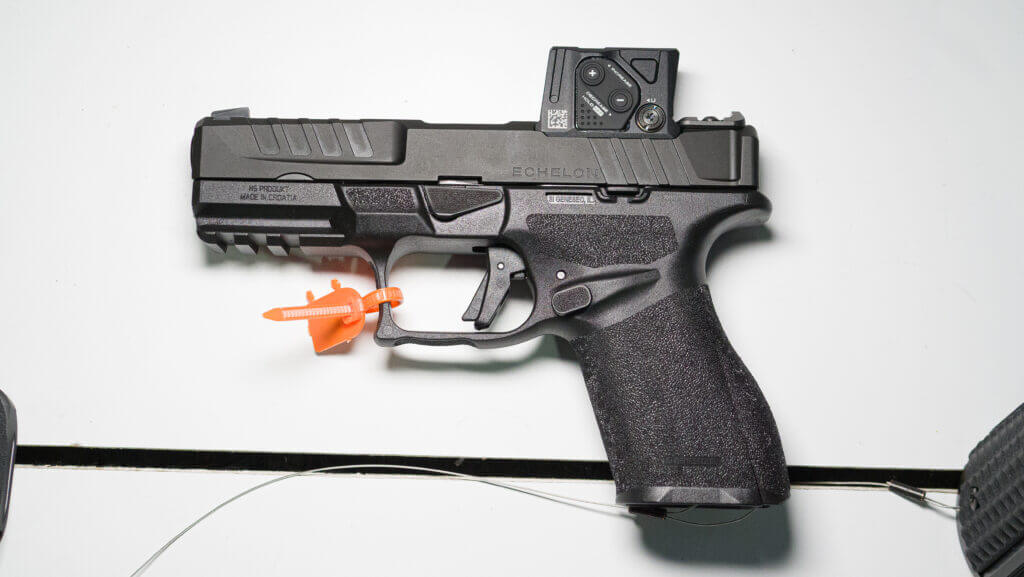 An Eschelon pistol lying on a white table facing left with COA sight attached.