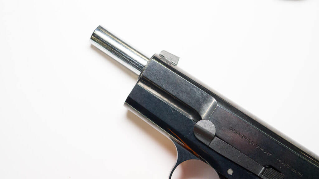 the stainless barrel protrudes from the front with the slide pulled back and gun on its left side facing left.