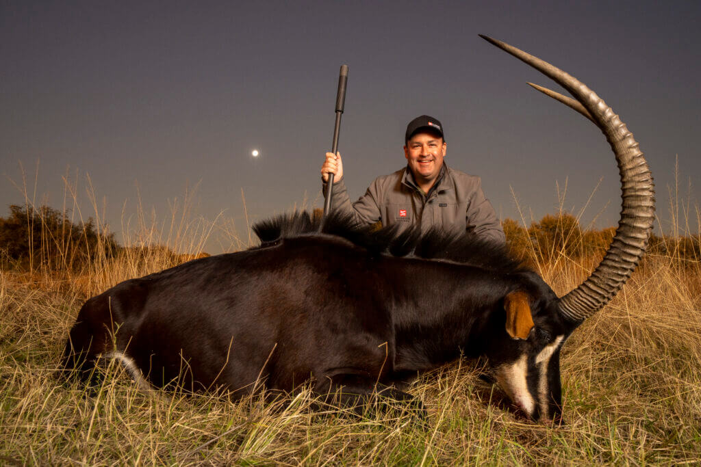 Brandon Maddox with suppressed rifle after a hunt at dusk in South Dakota grass