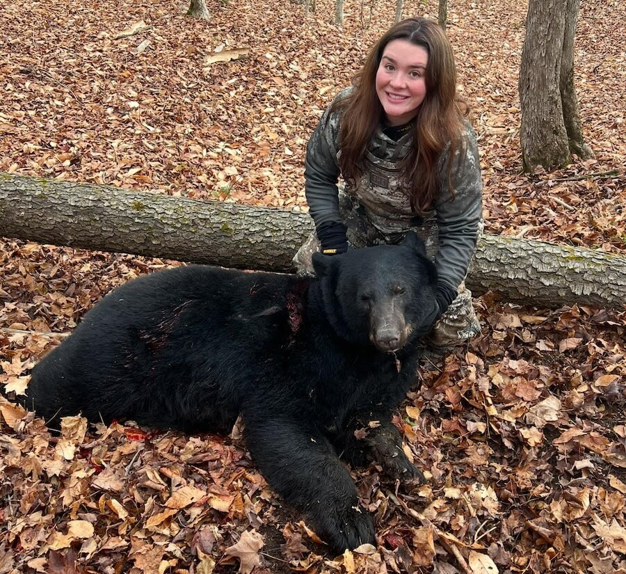 Hunter Janelle Miller kneeling beside her harvested black bear in the woods of Freedom, New York.