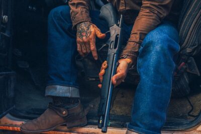 A man with tattooed arms holding a Henry Bear Leg's pistol.