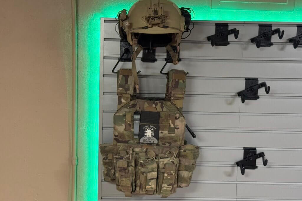Helmet and plate carrier mounts displayed on the Hold Up Displays modular Gun Wall
